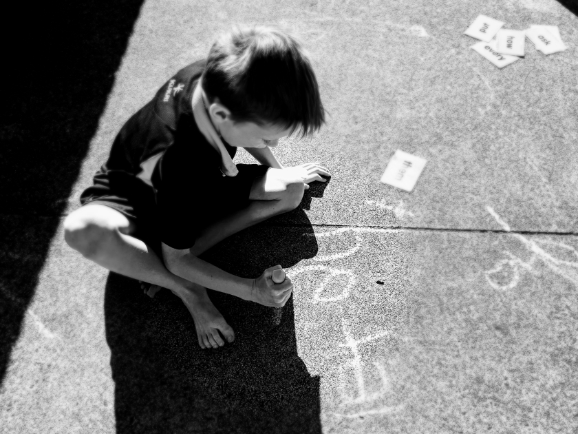 black and white photo of child drawing on pavement with chalk 